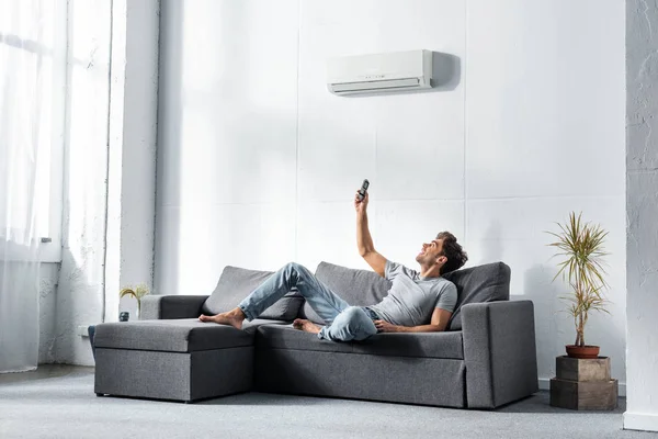 Knappe Man Liggend Bank Inschakelen Van Airconditioner — Stockfoto