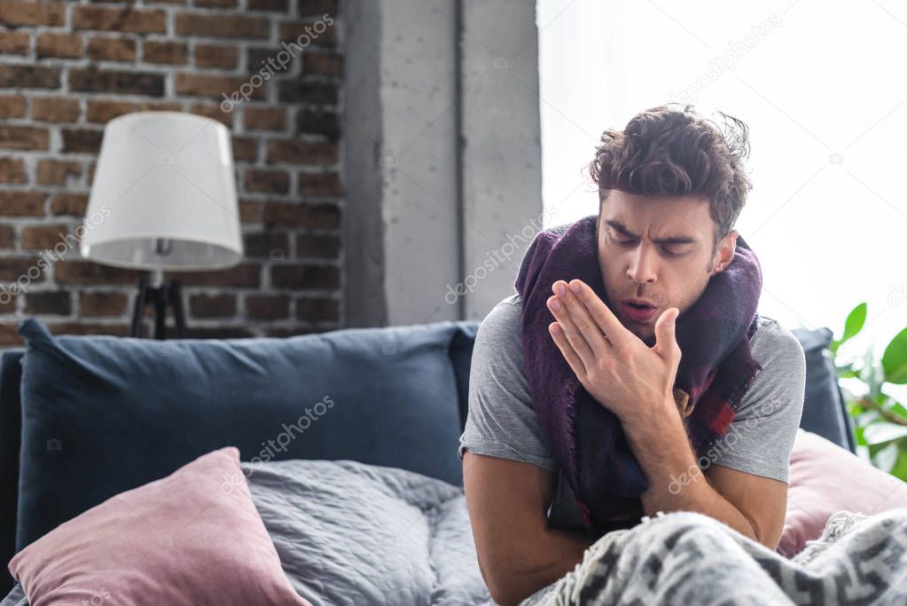 sick and handsome man in scarf coughing in bed 
