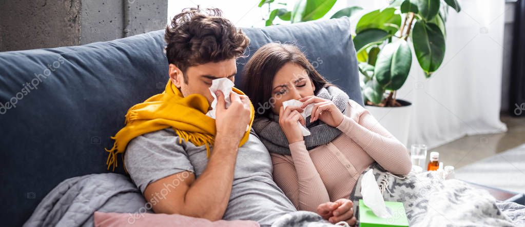 panoramic shot of sick girlfriend and boyfriend sneezing and holding napkins