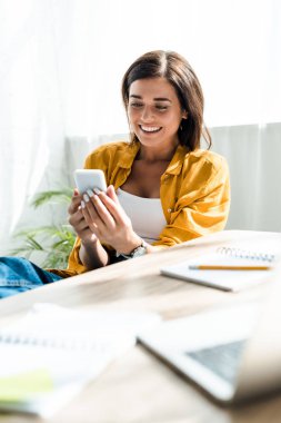Ofiste akıllı telefon kullanan güzel, neşeli bir serbest çalışan.