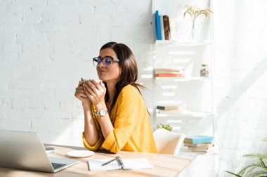 Güzel hayalperest serbest yazar ev ofisinde laptopuyla kahve molası veriyor.