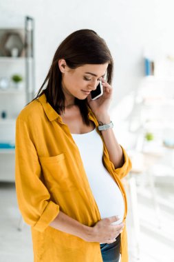 Sarı tişörtlü güzel hamile serbest çalışan ev telefonuyla konuşuyor.