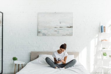 happy girl sitting with alarm clock on bed in the morning