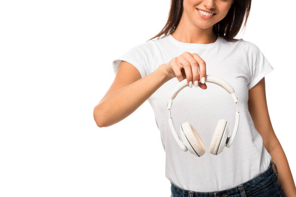 cropped view of young smiling woman holding headphones, isolated on white
