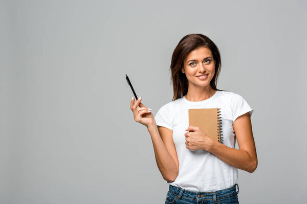 smiling young woman holding pen and notebook, isolated on grey