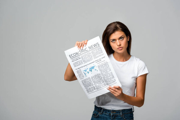 serious young woman showing economic newspaper, isolated on grey