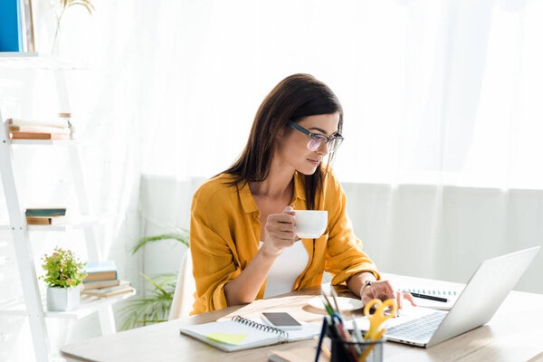 красивый фрилансер работает на ноутбуке с чашкой кофе в домашнем офисе
