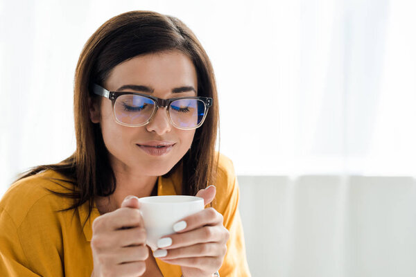 dreamy freelancer in eyeglasses having coffee break in home office