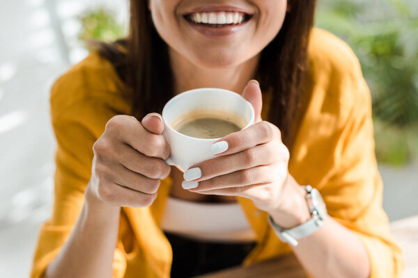 cropped view of smiling freelancer holding cup of coffee in home office