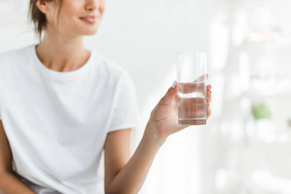 cropped view of smiling girl holding glass of water in the morning