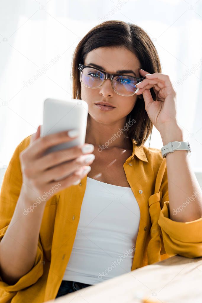 attractive confident freelancer in eyeglasses using smartphone in home office
