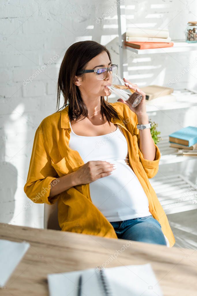 beautiful pregnant freelancer drinking water in home office