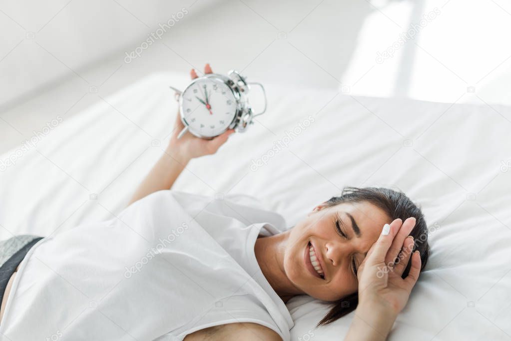 beautiful happy woman lying with alarm clock on bed in the morning