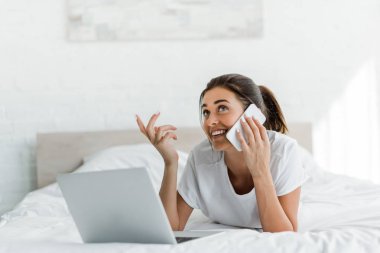 Neşeli kız akıllı telefonda konuşuyor ve sabahları dizüstü bilgisayar kullanıyor. 