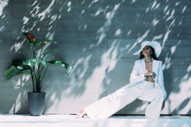 Beyaz takım elbiseli, şapkalı, poz veren ve dışarıda kameraya bakan çekici bir kadın. 