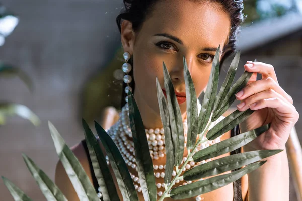 attractive woman in earrings with plant looking at camera