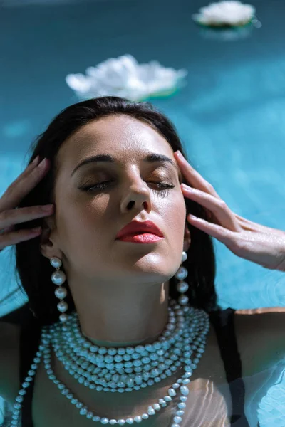 attractive woman in pearl necklace posing with closed eyes in pool