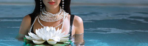 panoramic shot of woman in black swimsuit and pearl necklace posing in pool 