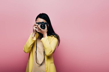 Sarı kıyafetli Asyalı kadın pembe üzerine izole edilmiş dijital kamerayla fotoğraf çekiyor.