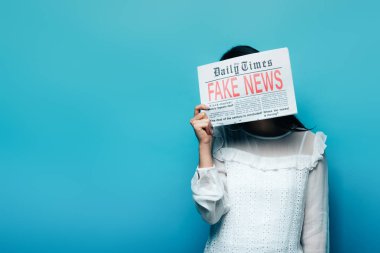 woman in white blouse holding newspaper with fake news on blue background clipart