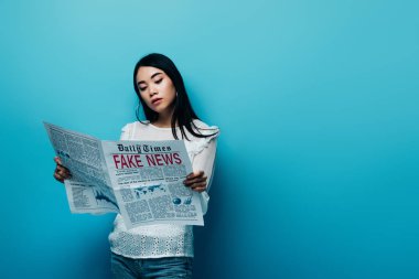 asian woman in white blouse reading newspaper with fake news on blue background clipart