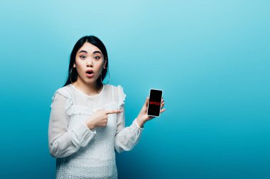 Kyiv, Ukrayna - 15 Temmuz 2019: mavi arka planda netflix uygulaması olan akıllı telefonu işaret eden Asyalı kadın