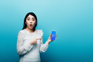 Kyiv, Ukrayna - 15 Temmuz 2019 - Asyalı kadın mavi arka planda Shazam uygulaması olan akıllı telefonu işaret ederek şok oldu