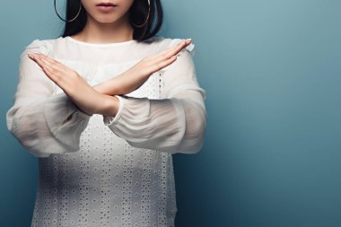 cropped view of brunette asian woman showinng stop gesture on blue background clipart