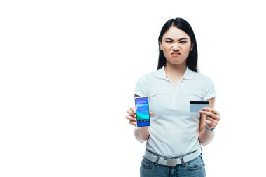 Hoşnutsuz esmer Asyalı kız kredi kartı ve akıllı telefon tutuyor. Kayıt uygulaması beyazdan izole edilmiş.