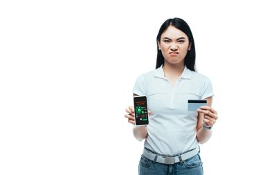 hoşnutsuz esmer Asyalı kız kredi kartı ve akıllı telefon tutuyor ve pazarlama analizi uygulaması beyazdan izole edilmiş.