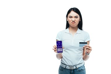Hoşnutsuz esmer Asyalı kız kredi kartı ve akıllı telefon tutuyor ve sağlık uygulaması beyazlara izole edilmiş.