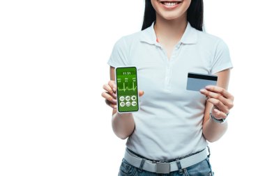 Gülümseyen esmer, Asyalı bir kızın elinde kredi kartı ve sağlık uygulaması olan akıllı bir telefon tutarken görüntüsü beyazlara izole edilmiş.