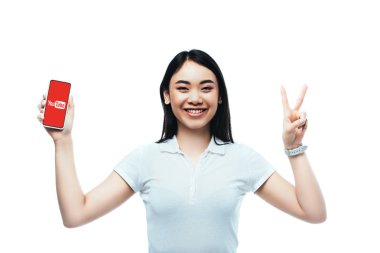 Kyiv, Ukrayna - 15 Temmuz 2019: mutlu esmer Asyalı kadın Youtube uygulaması ile akıllı telefon tutuyor ve barış işareti beyaz üzerinde izole ediliyor