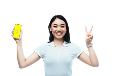 Kyiv, Ukrayna - 15 Temmuz 2019: mutlu esmer Asyalı kadın Snapchat uygulaması ile akıllı telefon tutuyor ve beyaz üzerinde barış işareti gösteriyor
