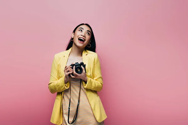 穿着黄色衣服的兴奋的亚洲女人拿着用粉色隔离的数码相机 — 图库照片