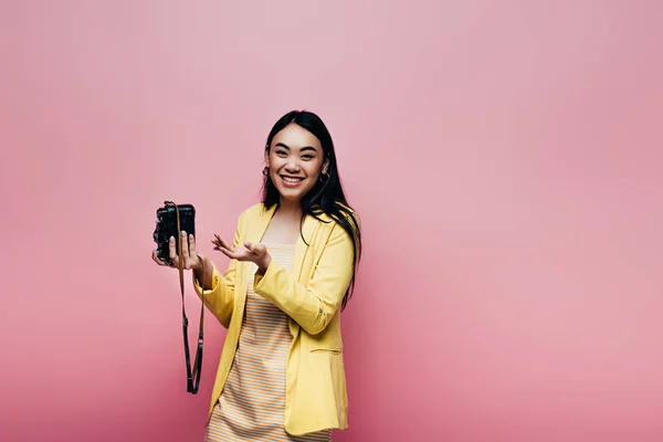 穿着黄色衣服的快乐的亚洲女人拿着用粉色隔离的数码相机 — 图库照片