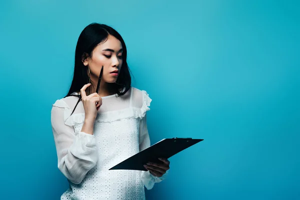 Nachdenklicher Asiatischer Journalist Weißer Bluse Mit Klemmbrett Auf Blauem Hintergrund — Stockfoto