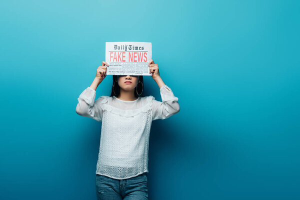 asian woman in white blouse holding newspaper with fake news on blue background