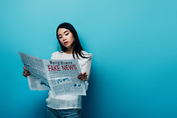 asian woman in white blouse reading newspaper with fake news on blue background