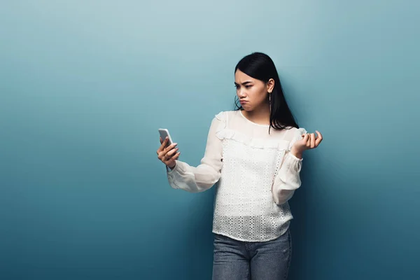 Δυσαρεστημένη Ασιάτισσα Άσπρη Μπλούζα Που Κρατάει Smartphone Μπλε Φόντο — Φωτογραφία Αρχείου