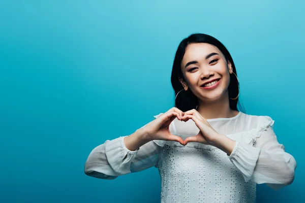 Gelukkig Brunette Aziatische Vrouw Tonen Hart Met Handen Blauwe Achtergrond — Stockfoto