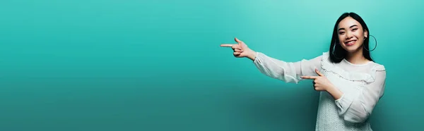 Happy Brunette Asian Woman Pointing Fingers Turquoise Background Panoramic Shot — Stock Photo, Image