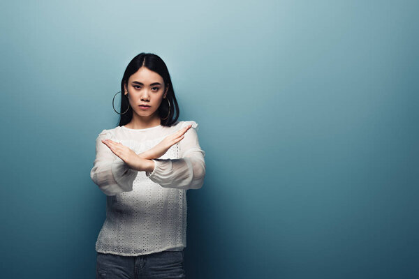 upset brunette asian woman showing stop gesture on blue background