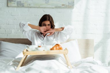 Beyaz gömlekli çekici bir kadın sabah kahvaltısını yatakta yapıyor. 