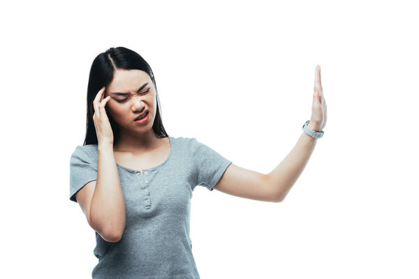 attractive asian girl suffering from headache and showing stop gesture isolated on white