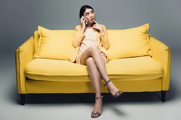 Pensive Asian Businesswoman Sitting Yellow Sofa Crossed Legs Talking Smartphone — Stock Photo, Image
