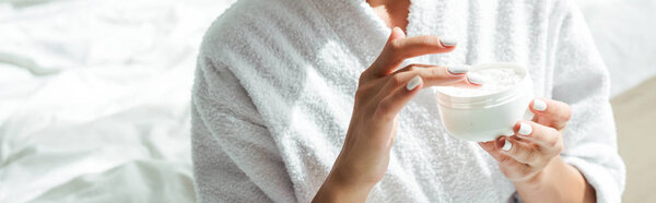 panoramic shot of woman in bathrobe holding cosmetic cream at morning 