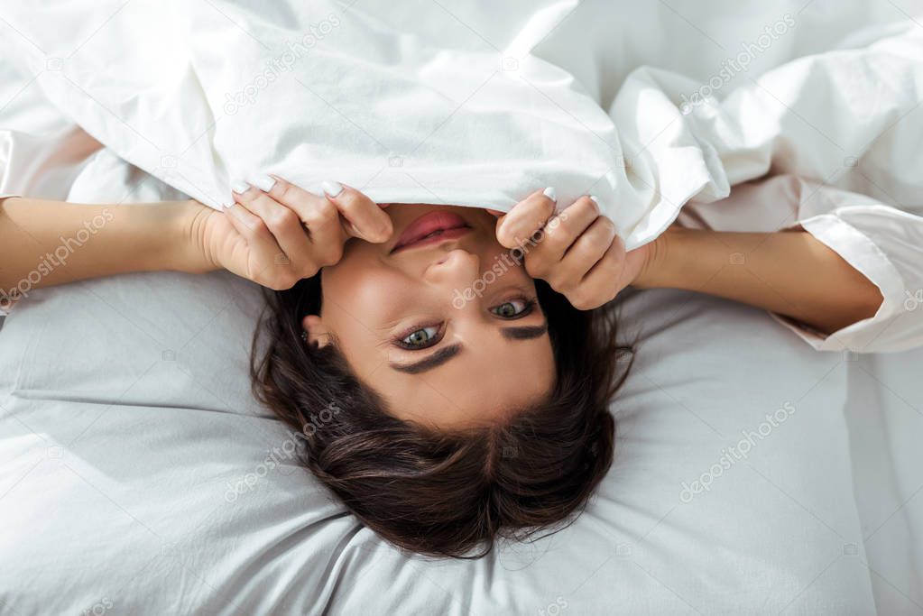 top view of attractive woman holding blanket and looking at camera at morning 