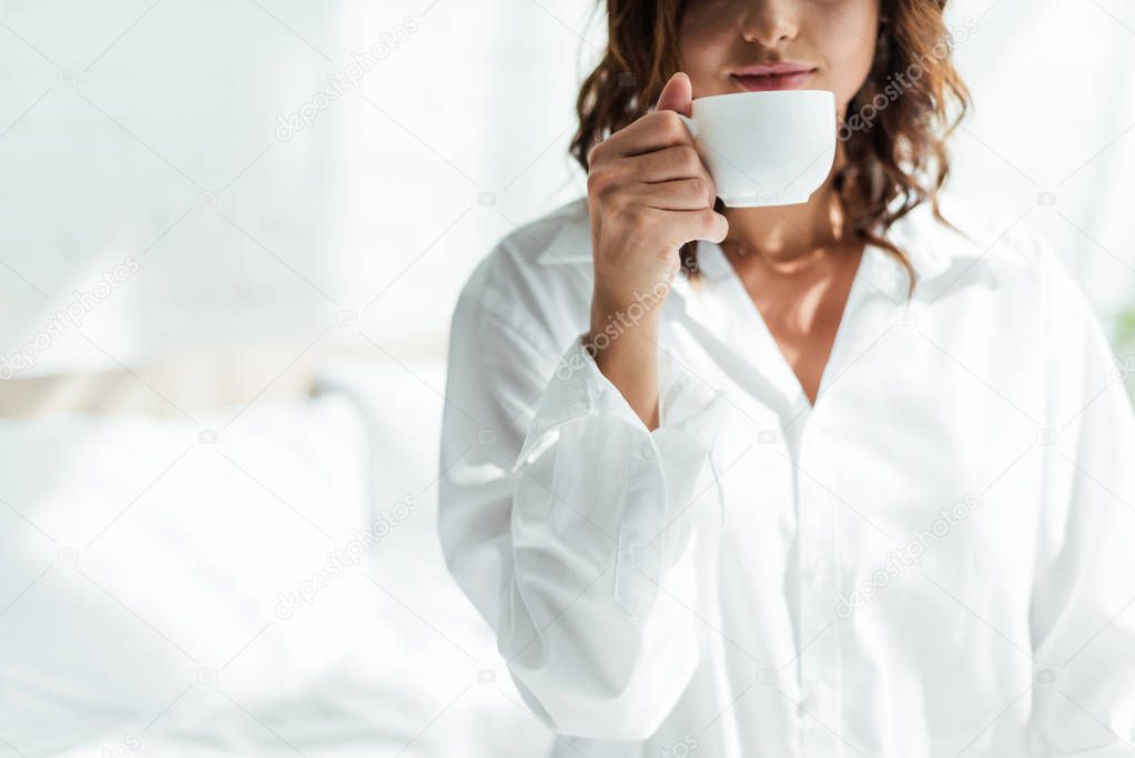 cropped view of woman in white shirt holding cup at morning 