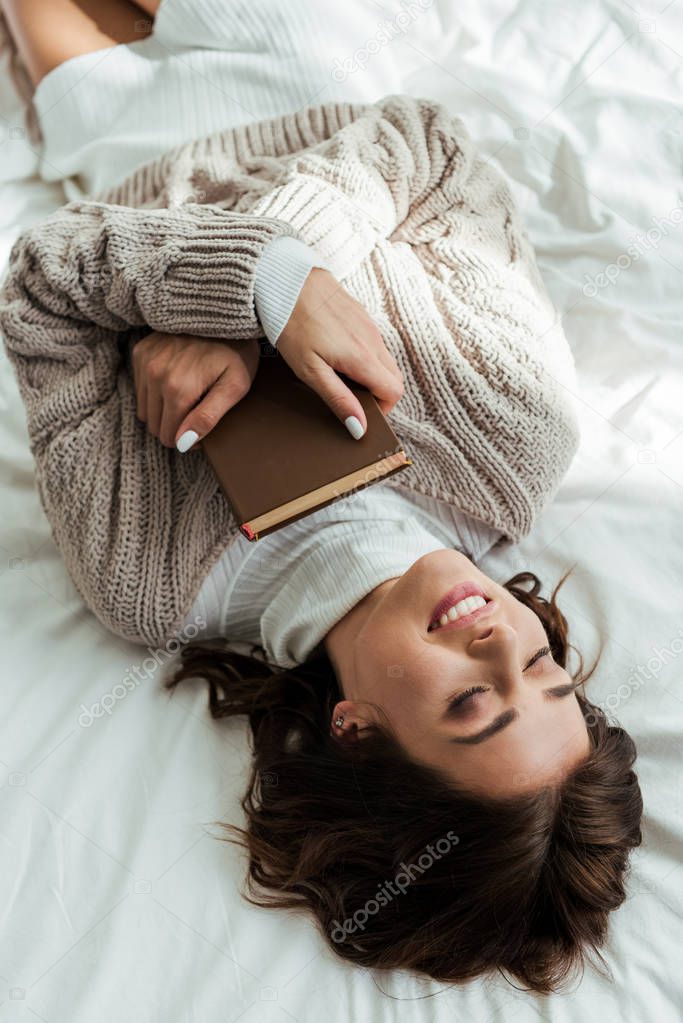 high angle view of smiling woman in sweater lying in bed at morning 